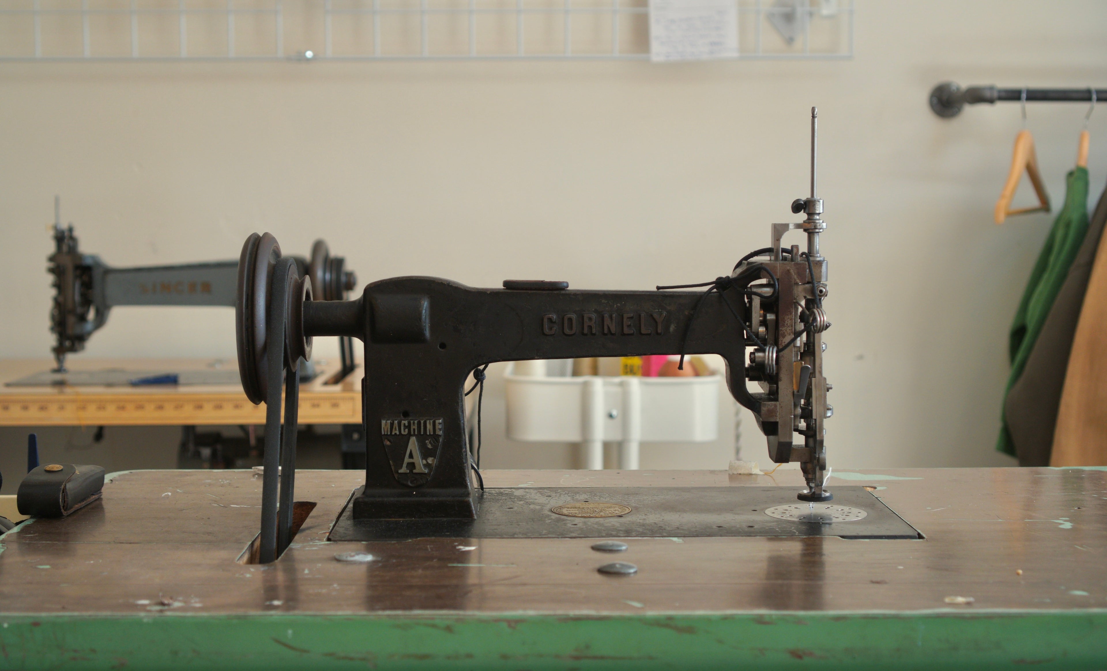 A Cornely chainstitch embroidery machine sitting on a vintage sewing machine table. In the background is a singer 114w103 chainstitch embroidery machine.