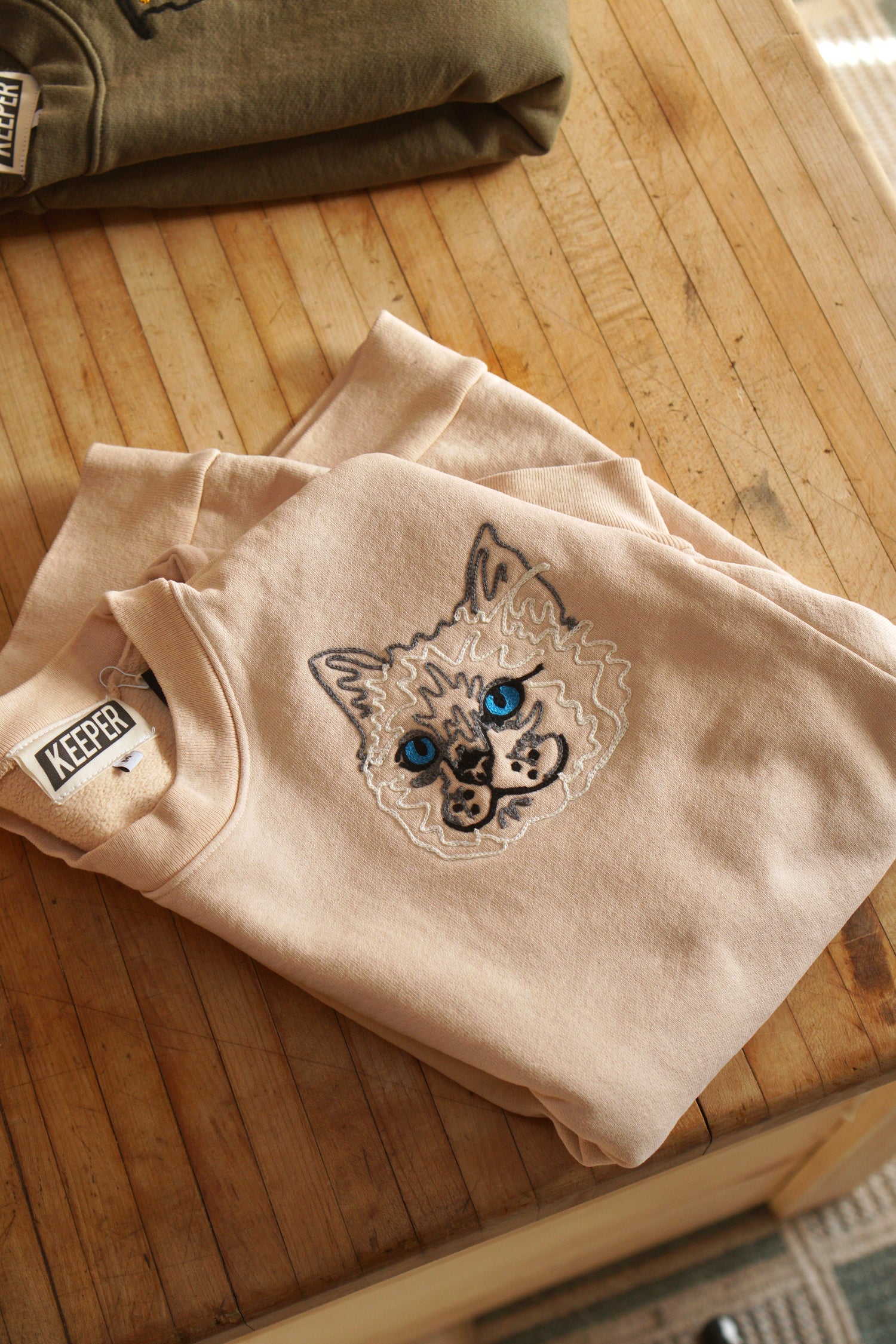 A crewneck sweatshirt with a portrait of a white cat embroidered.
