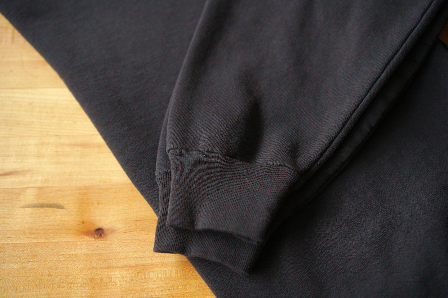Close up picture of a folded black sweatshirt. This picture is showing the cuffs of the sweatshirt arms. 