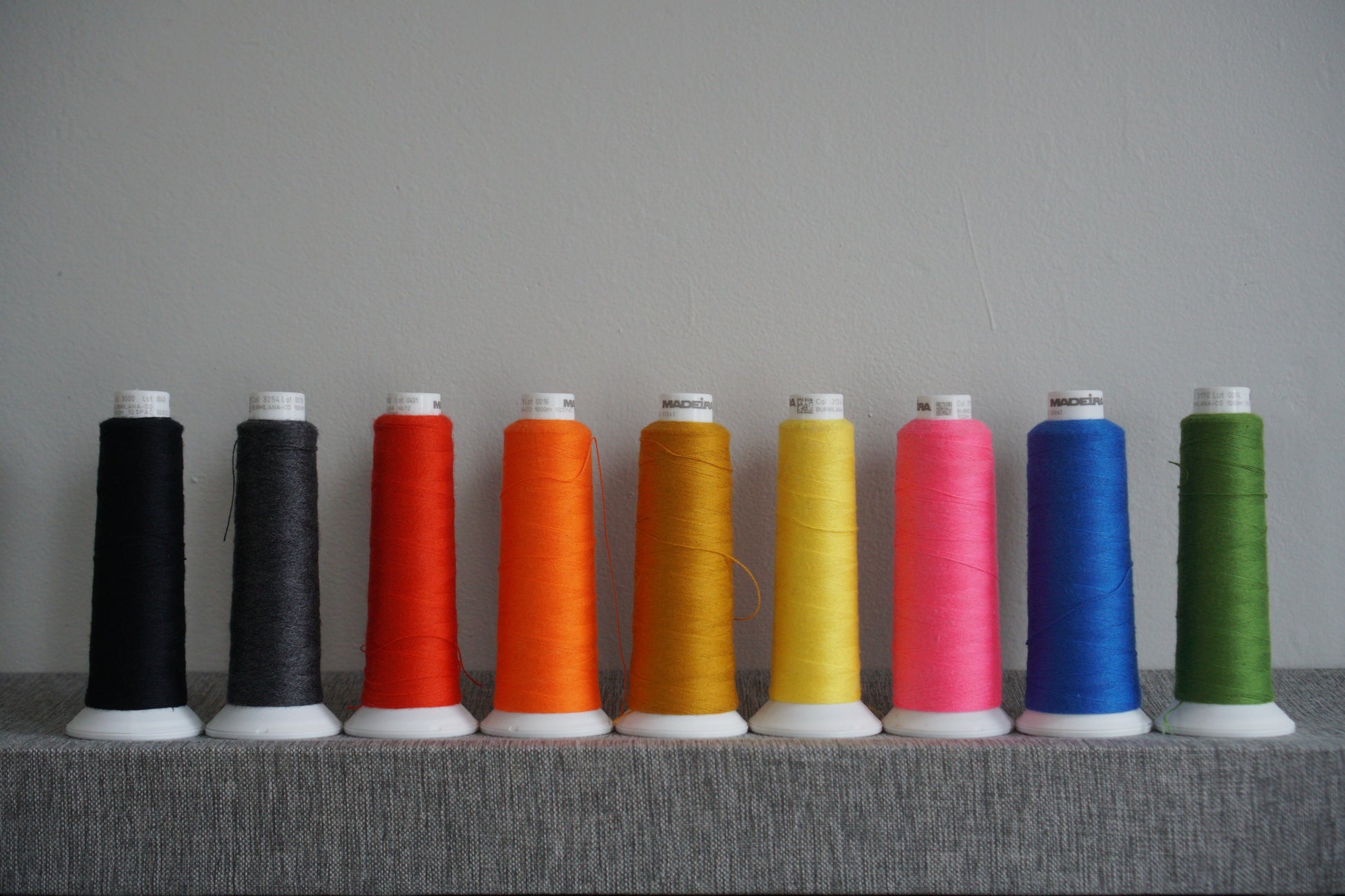 Row of colorful spools of thread on a gray surface with a gray background